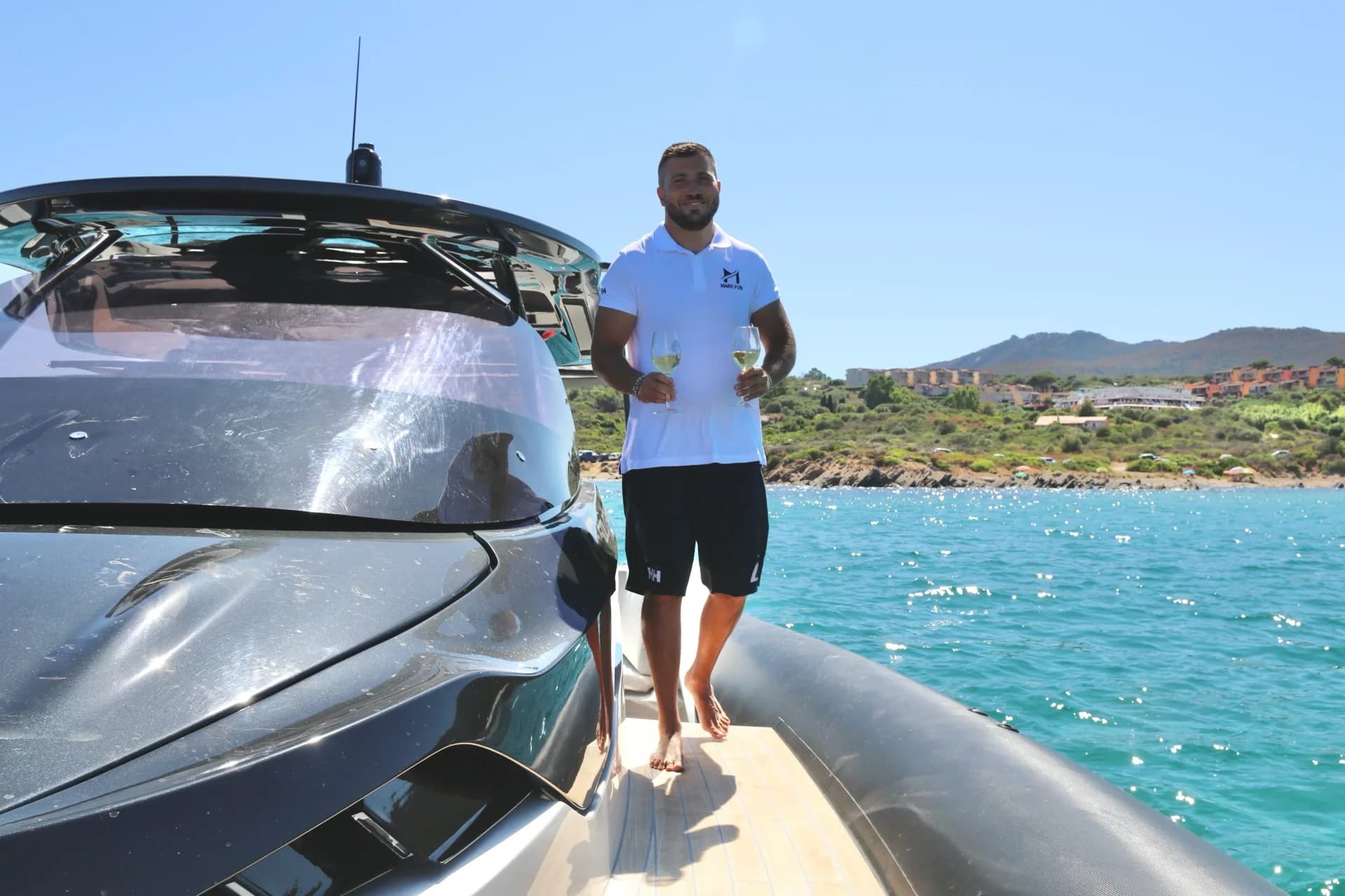 Carlo from MareFun standing on the bow of a charter boat in turquoise Sardinian waters